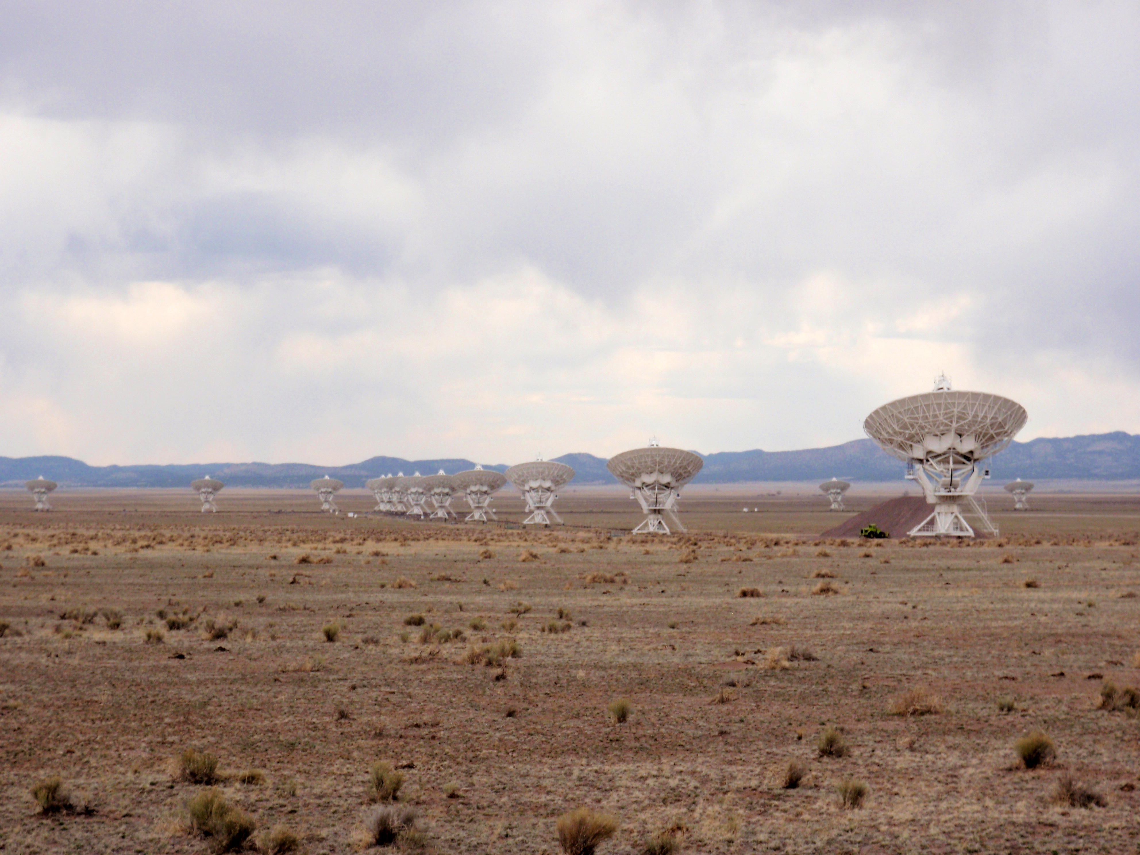 A row of large white parabolic radio-telescope dishes on a desert plain.